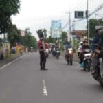 Petugas Polsek Tikung membantu warga menyeberang saat melaksanakan program Commander Wish Pagi di simpang tiga depan Mako Polsek Tikung, Lamongan.